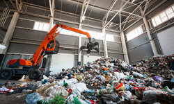 Abfälle rechtssicher entsorgen – Abfallrecht für gewerbliche und industrielle Abfallerzeuger Grabbing excavator collects garbage in plant warehouse